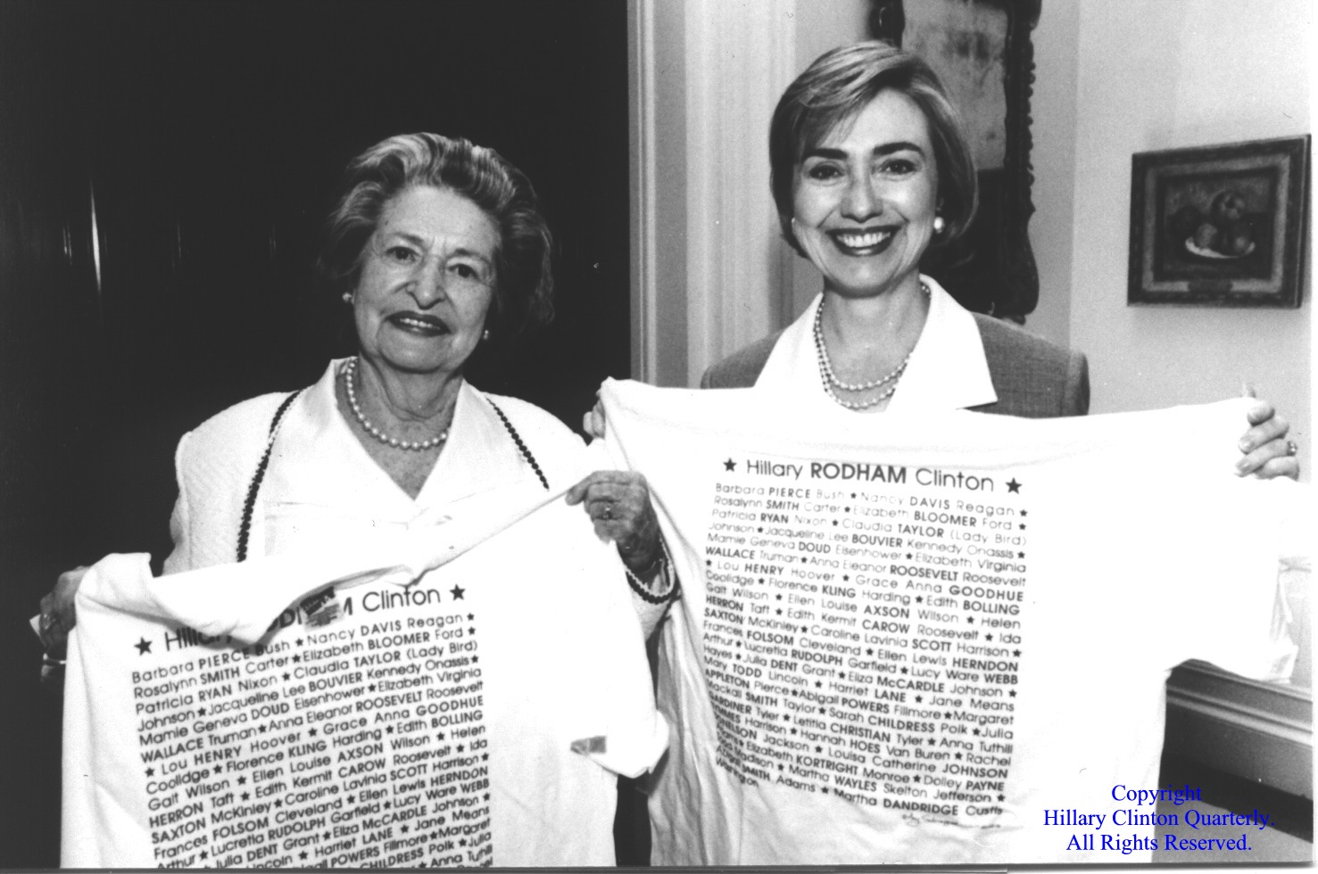 Lady Bird Johnson and Hillary Clinton holding up tee-shirts with the names of all the First Ladies, 1994.