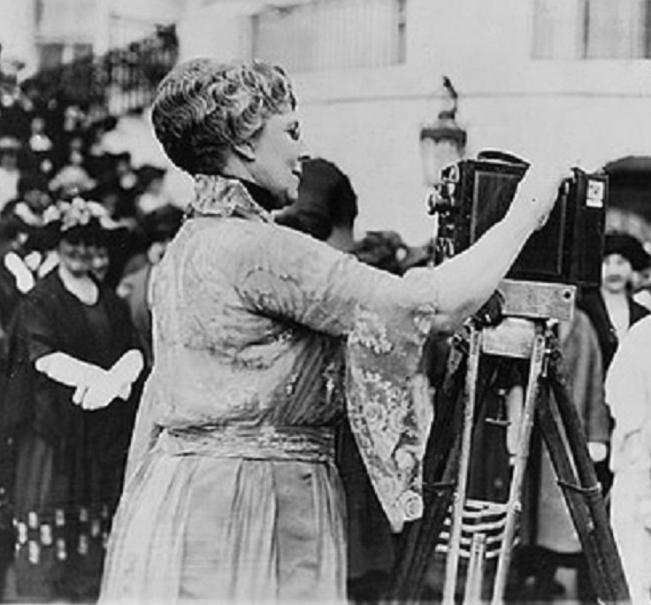 First Lady Florence Harding cranks out a newsreel camera before a group of women press.
