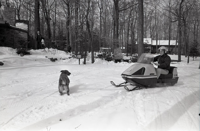 President Ford snowmobiling at Camp David as his dog Liberty looks on.